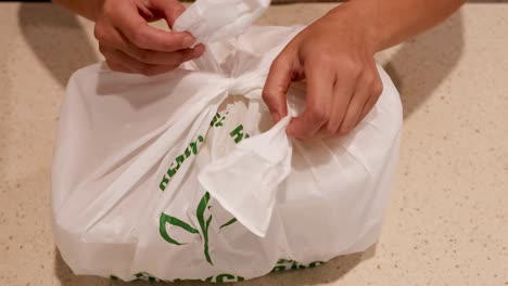 hands carefully open a recyclable bag, revealing a container inside on a kitchen countertop.