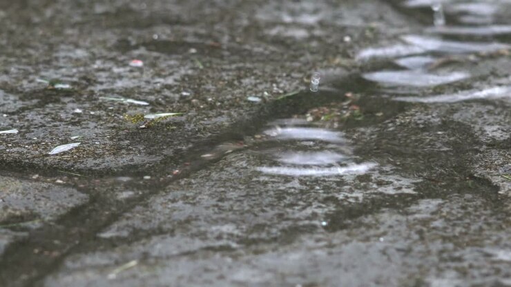Charco en camino empedrado y gota de agua de lluvia cayendo sobre él. 4K.