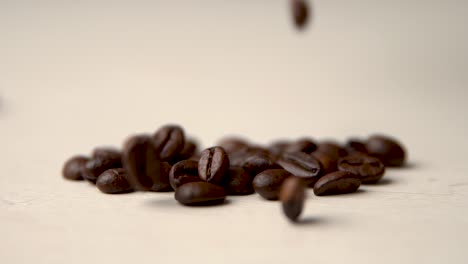 roasted coffee beans fall from above on a beige surface slow motion