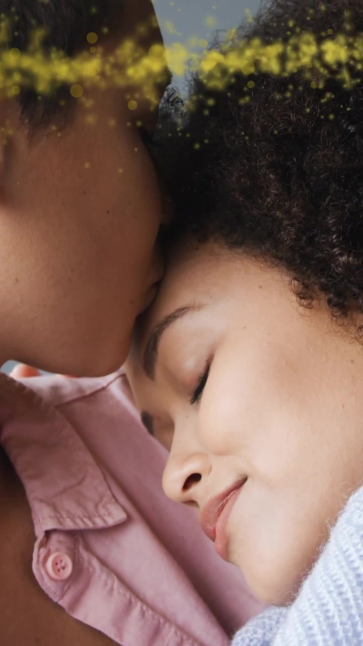 Video verticale: Due donne, una inclina la testa e coccola la partner, scintille dorate che fluttuano, romanticismo.