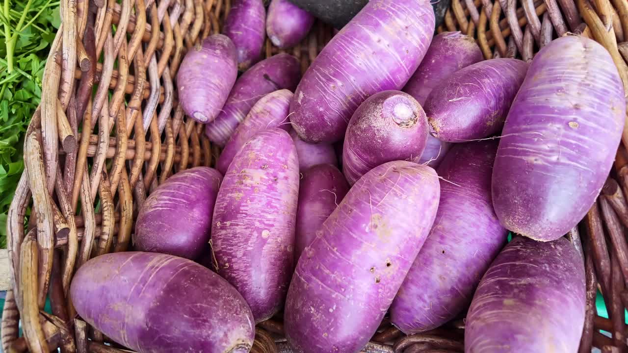 Overhead closeup of purple radishes and black radish arranged in wicker basket
