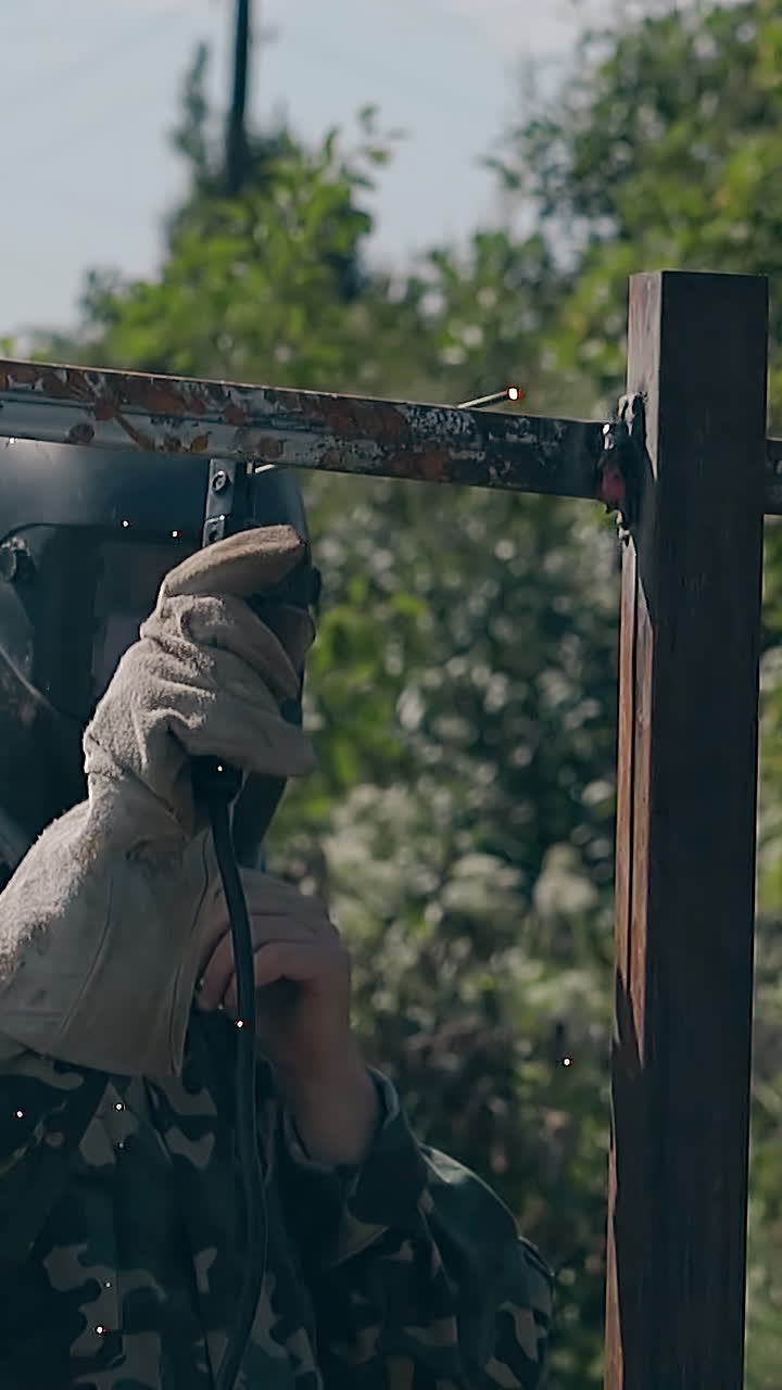 slow motion professional welder fixes carcass of new fence in country house yard on sunny day
