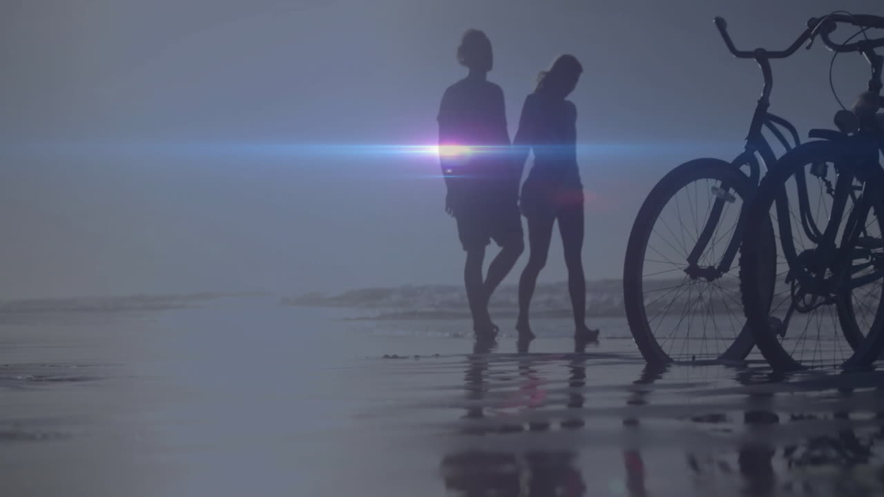 Walking on beach near bicycles, people silhouetted with lens flare effect