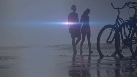 walking on beach near bicycles, people silhouetted with lens flare effect