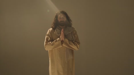 Three-Quarter-Length-Studio-Portrait-Of-Man-Wearing-Robes-And-Sandals-With-Long-Hair-And-Beard-Representing-Figure-Of-Jesus-Christ-Praying-2