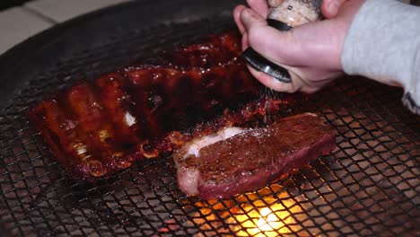 caucasian hands grind salt on tasty steak grilling on barbecue braai