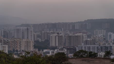 time lapse of sun setting behind mountains and day to night transition of cityscape, maharashtra, india