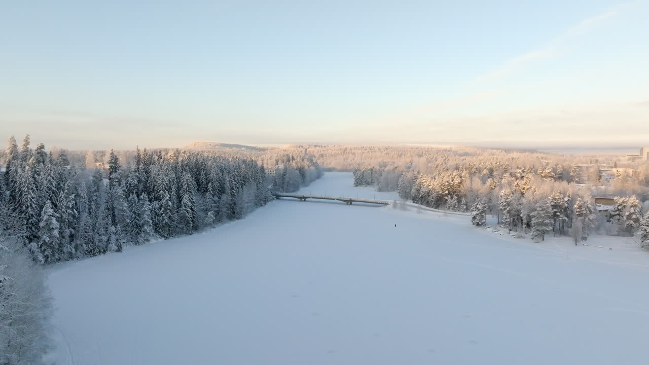 Aerial tracking shot over snowy bridge, in middle of frosty forest, winter sunrise