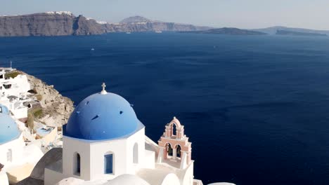 blue domed church at oia on santorini with fira in the distance