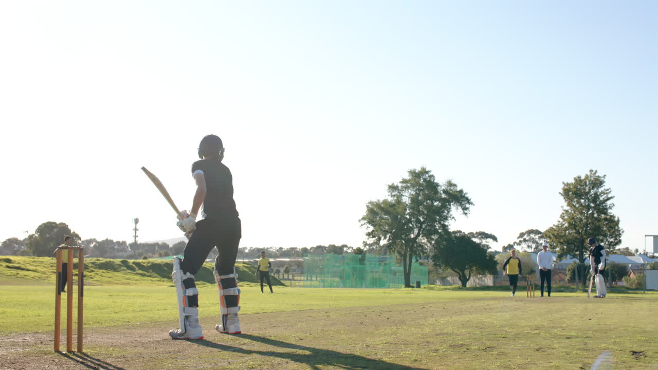 Two teams of multiracial male cricket players and male umpire playing cricket on pitch
