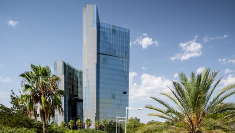 barcelona mirrored glass skyscraper with clouds in the sky and wind blowing palm trees