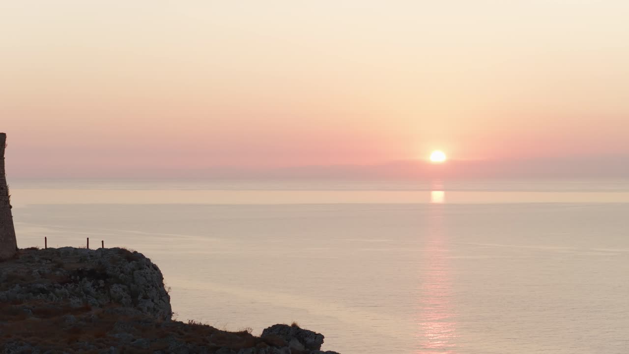 Historic Torre Minervino, ancient coastal watchtower ruin, silhouetted with beautiful sunrise over calm sea in background, Puglia, Italy. Aerial drone lateral view, copy space