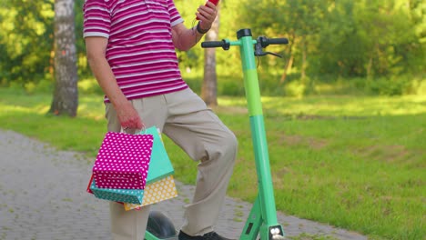 caucasian old senior grandfather man leaning on electric scooter after shopping with colorful bags