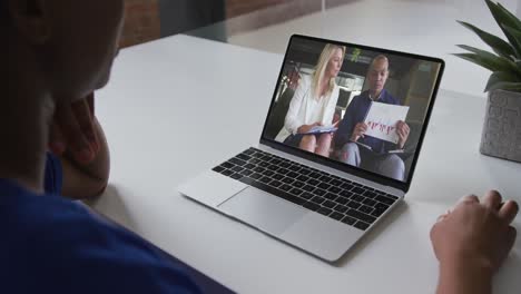 African-american-woman-talking-on-video-call-on-laptop-with-male-and-female-office-colleague-at-home