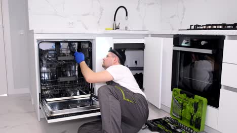 a professional repairman in overalls checks a household dishwasher in the kitchen
