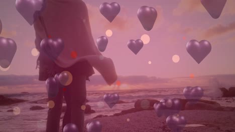 animación de corazones púrpuras sobre pareja enamorada en la orilla del mar