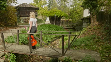 junge weibliche gitarristin geht ruhig über eine hölzerne brücke in einem rustikalen dorf