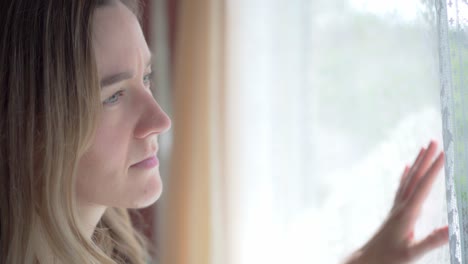 sad girl inside house looks out through window with white lace curtains, close up