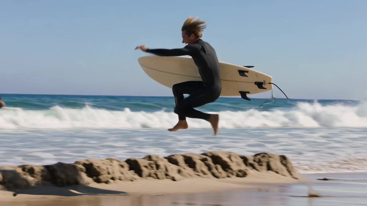 Un uomo in muta avvista le onde, corre sulla spiaggia con la sua tavola da surf corta, salta una cresta e atterra ridendo.