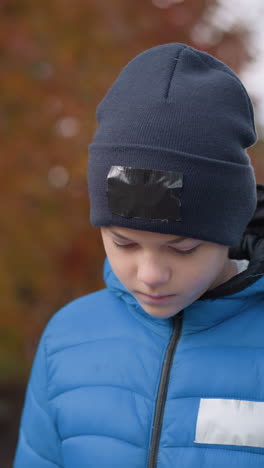 niño con chaqueta azul y gorra negra caminando con la cabeza inclinada pensativamente, árboles de otoño en el fondo borroso, estado de ánimo reflexivo en un paseo por el vecindario