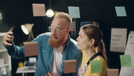 business couple making stupid faces on mobile camera selfie in hipster office