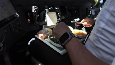 arm and hand of a white pilot inside a jet cockpit eating his crew meal in flight