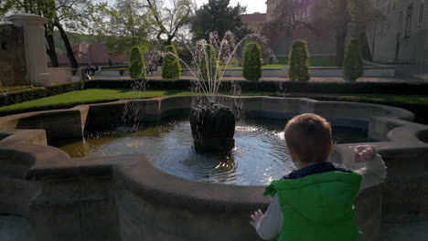 Nahaufnahme-Eines-Kleinen-Jungen-In-Zeitlupe,-Der-Zum-Brunnen-Rennt-Und-Münzen-Ins-Wasser-Wirft,-Prag,-Tschechische-Republik