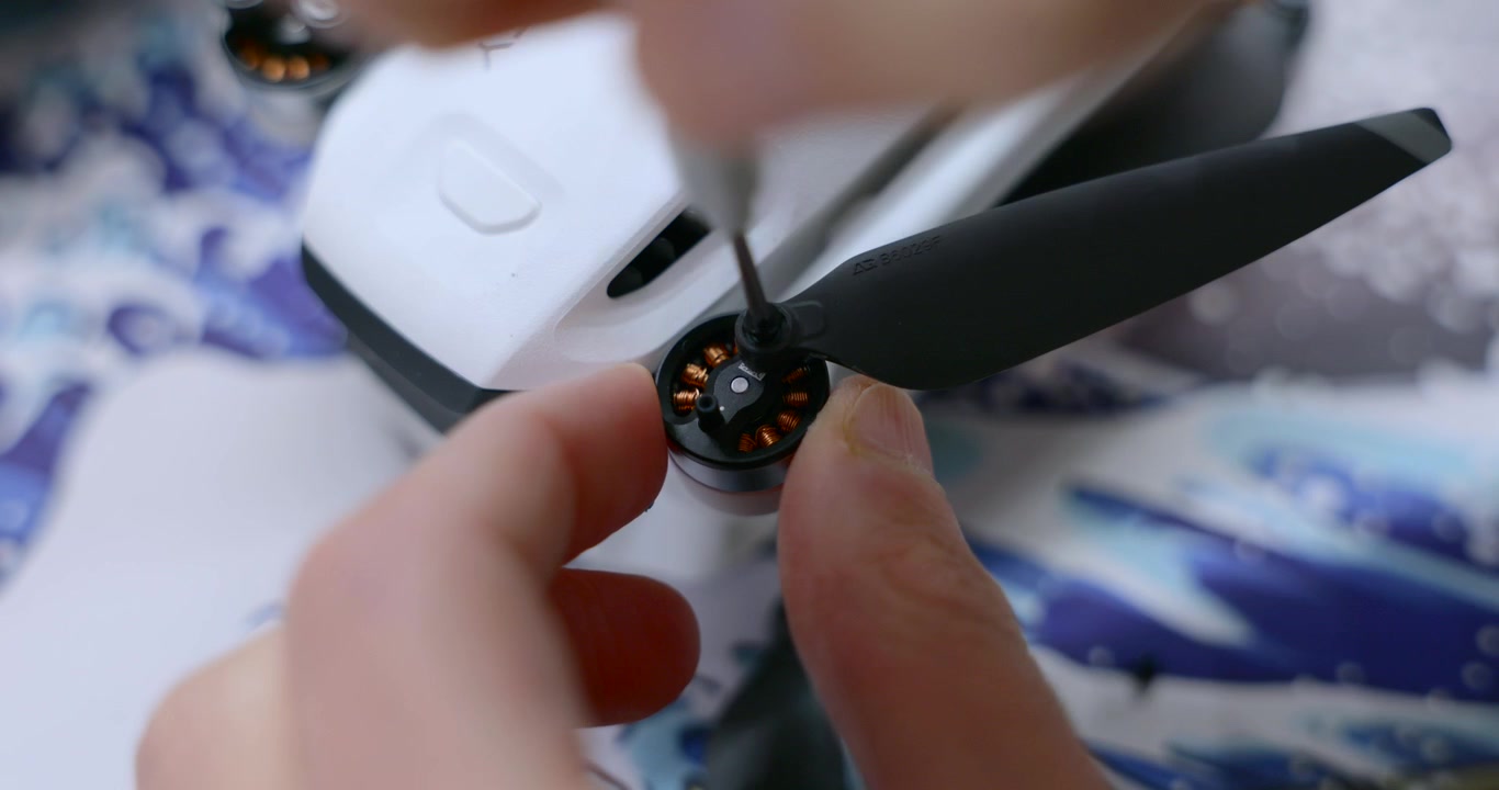 Hands meticulously assemble a drone, screwing a propeller blade onto the motor for flight.
