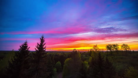 time lapse of golden and blue hour with multi-colored clouds and at sky - epic sunrise in rural landscape with trees and bush in foreground