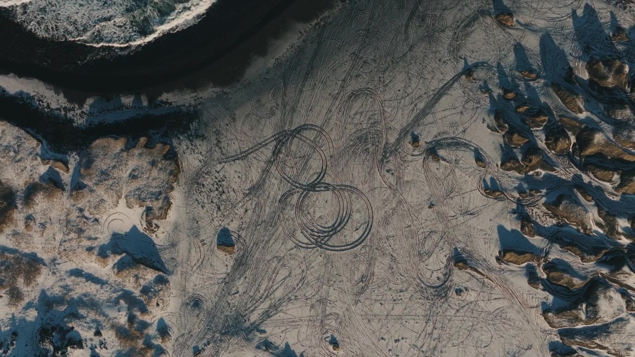 Top Down Aerial of Tire Tracks on Snowy Black Sand Beach