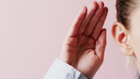detalle de video de una mujer caucásica cubriendo la mano detrás de la oreja para escuchar más claramente, con espacio de copia rosa