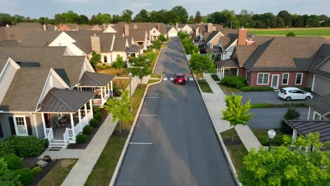 Aerial-view-of-a-red-car-in-motion-on-the-road-between-houses-and-homes-in-American-neighborhood