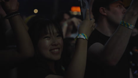 multi ethnic group of people dancing and taking photos of a band in a live rock concert