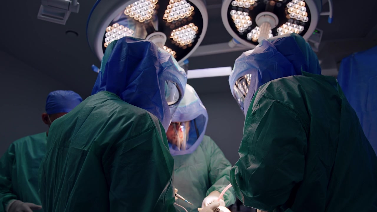 L'équipe chirurgica esegue l'intervento. Il chirurgo principale utilizza dispositivi chirurgici durante l'operazione. Vista dal basso sui medici con caschi protettivi