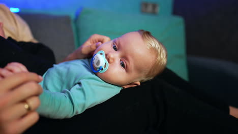 lovely child with fair hair lies on mom's laps. mother takes a pacifier out of kid's mouth and waves it in front of child's face. close up.