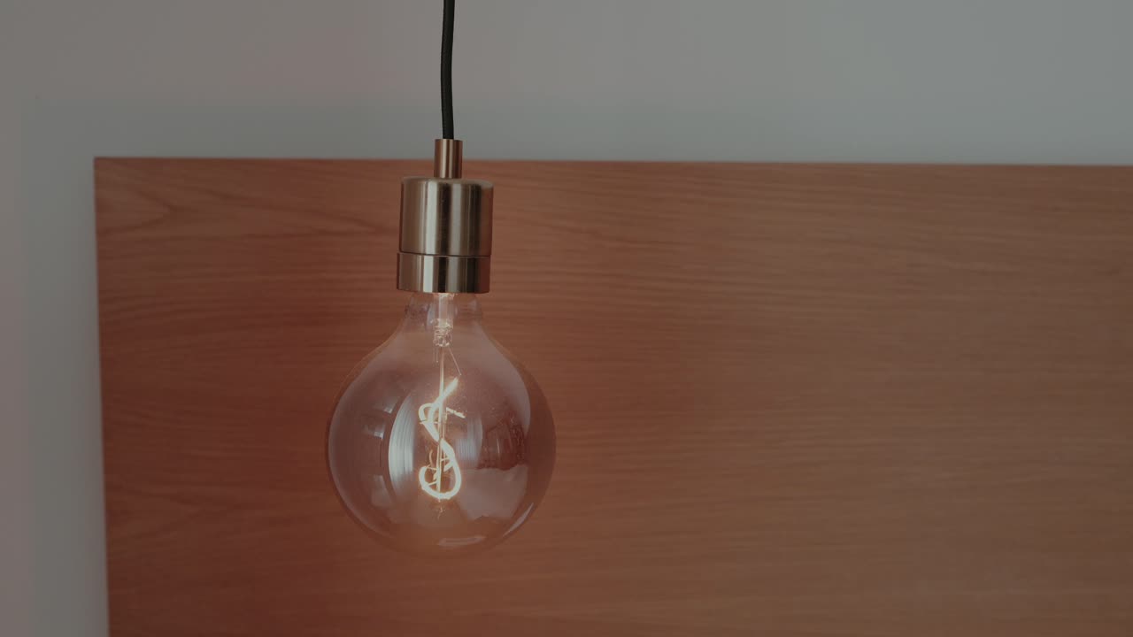 vintage style light bulb gently swaying with soft warm glow against wood and white wall