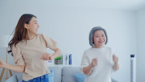 asian funny senior old mom and daughter dance together in living room. attractive beautiful woman and mature grandma feel happy to spend leisure time at home, enjoy listen to music on weekend in house