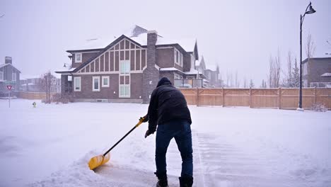 50 to 60 year old male shovelling snow out of a driveway after a winter blizzard