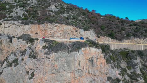 A-truck-driving-along-a-scenic-coastal-cliffside-road-in-port-ginesta-barcelona,-aerial-view