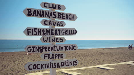 un cartel en una playa de arena tropical que muestra direcciones para diferentes lugares para comer y beber