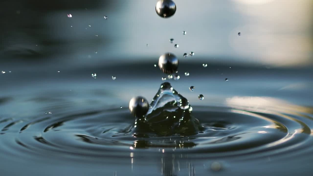 Dritter metallischer Tropfen tritt in Säule ein, trifft Wasseroberfläche, erzeugt Krone und Wellen.