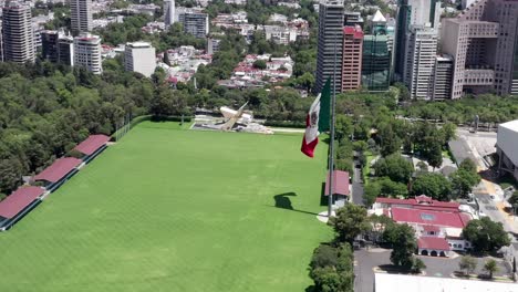 flight above empty, desolate, deserted and closed campo marte green grass venue with patriotic mexican flag waving in wind, mexico city, covid-19 pandemic, lockdown and quarantine, overhead aerial