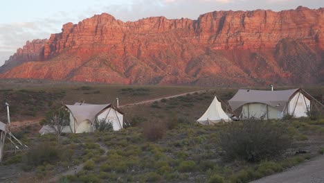 canvas tents in utah with red rock cliffs in background during sunset