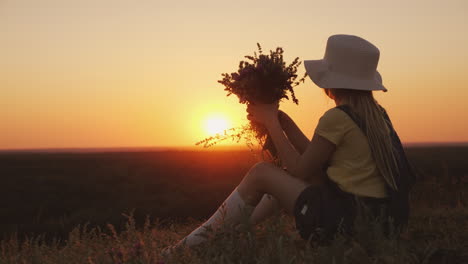 a girl in a hat admires the sunset in a picturesque place she sits on a hill her chin on her hands b