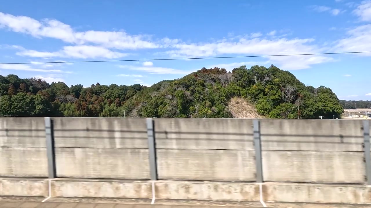 Toma en movimiento desde un vehículo pasando barreras de hormigón y colinas verdes bajo cielos azules.