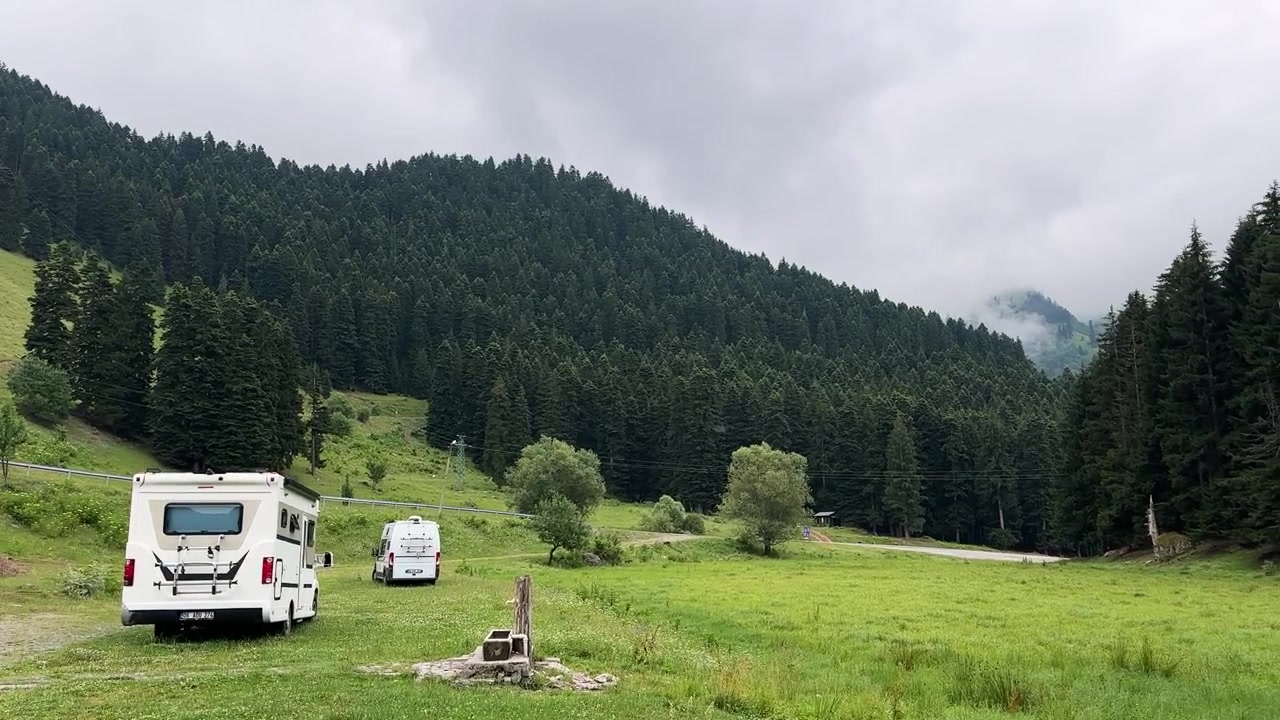 Meraviglioso campeggio panoramico per van life in un tranquillo campo verde, Savsat. Paesaggio panoramico di pineta, campagna primaverile, montagna nuvolosa. Avventura di coppia in caravan/camper in Turchia, turismo.