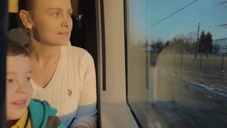 Small-boy-with-mother-sitting-against-window-in-their-rail-train-place-and-watching-outside