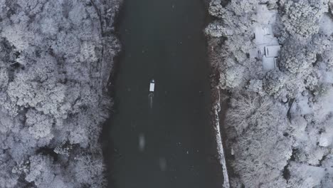 Boat-travels-up-Katsura-River-in-the-snow,-Top-Down-Aerial-View-in-Winter-Scene