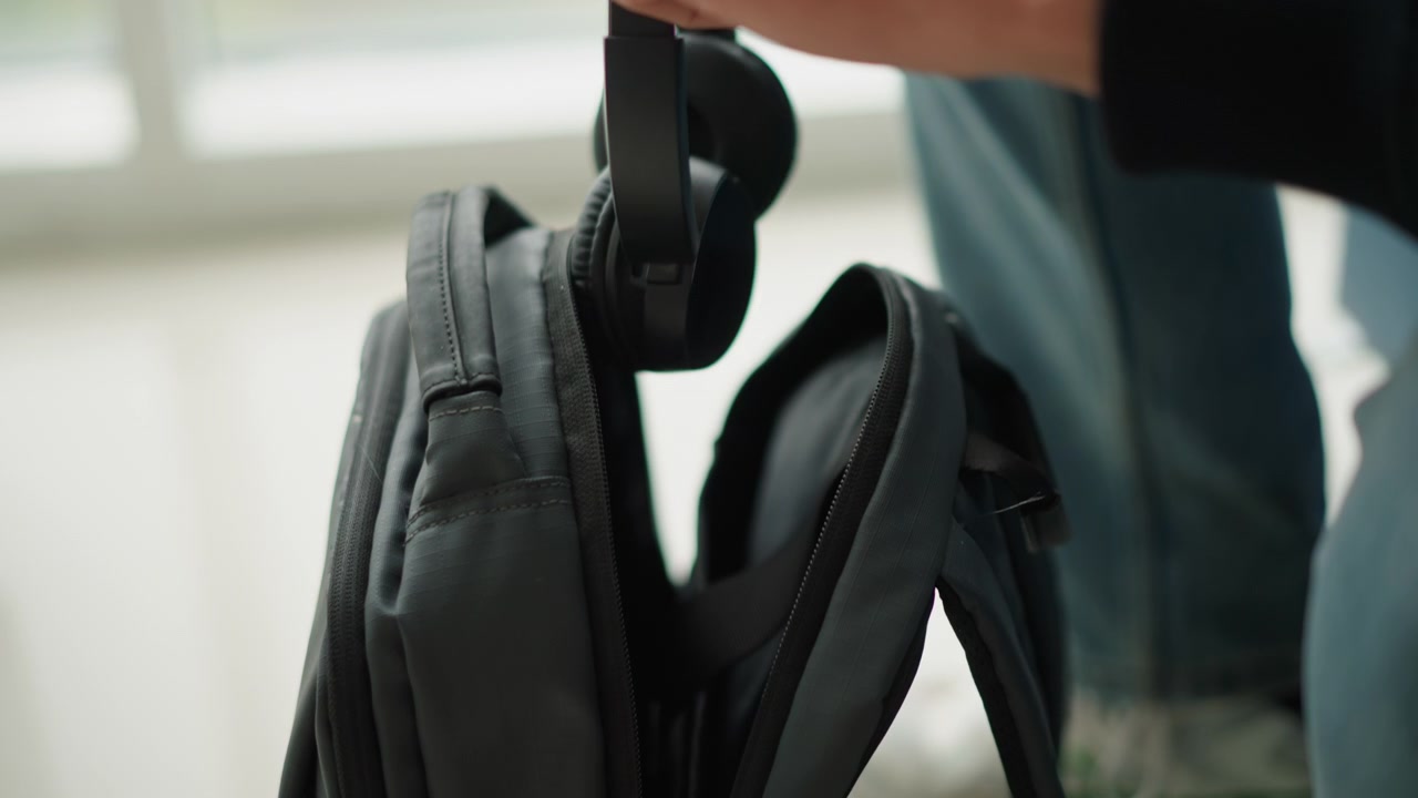Nahaufnahme der Hände einer Person, die die Reißverschlüsse von zwei schwarzen Stoffrucksäcken öffnet und deren Innenfächer enthüllt. Die Person greift dann in eine Tasche, um verschiedene persönliche Gegenstände herauszuholen und zu untersuchen.