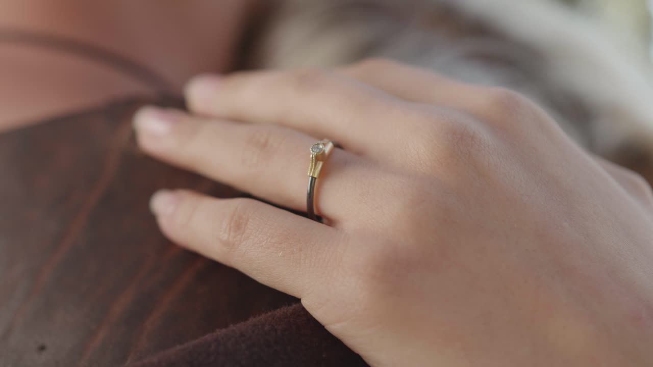 Close-up of a woman's hand with a beautiful engagement ring resting gently on a shoulder. Intimate, romantic scene showing love, affection, and commitment. The ring is black gold